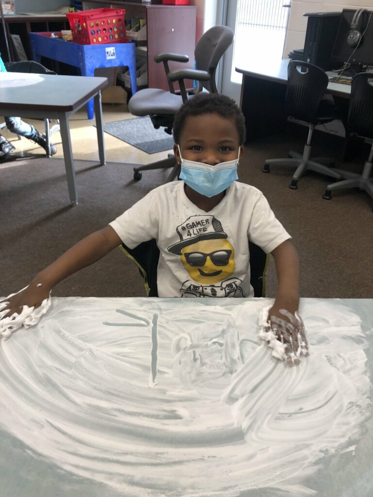 A student writing letters in the shaving cream.