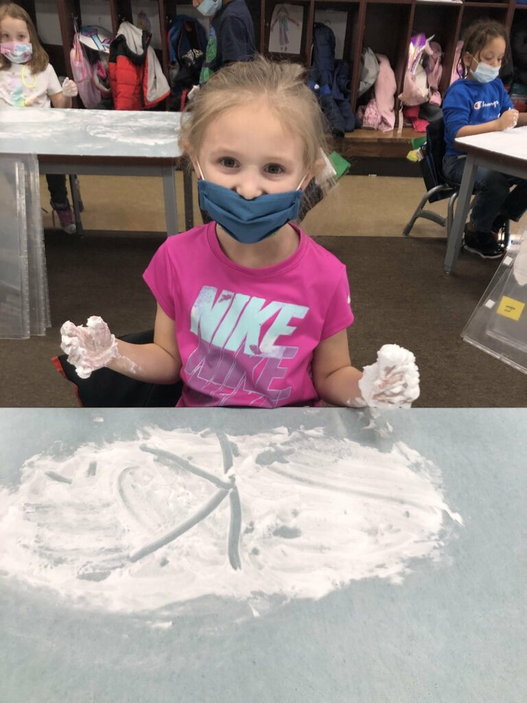 A kindergarten student writes in the shaving cream.