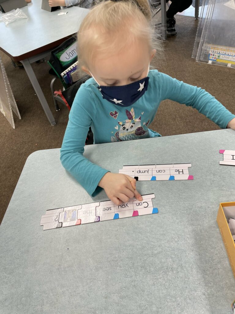 A kindergarten student using puzzle pieces of letter sounds to build words.