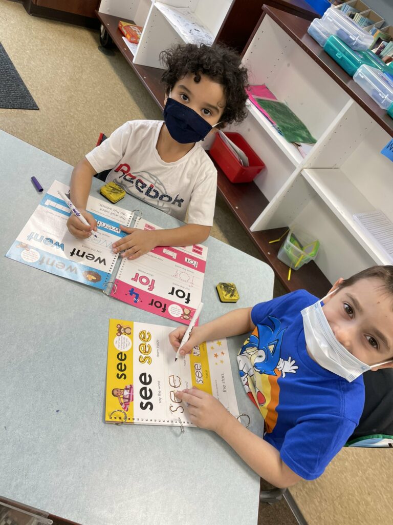 Two kindergarten students sit together and practice writing words.