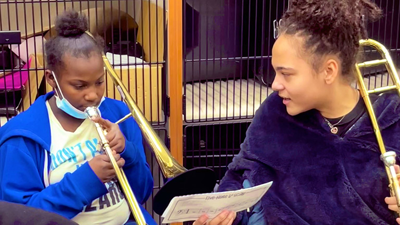 An eighth grade trombone player giving a sixth grader some tips.