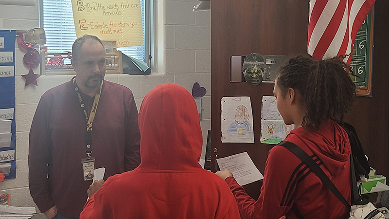 Two eighth grade students read a note of appreciation to their former third grade teacher.