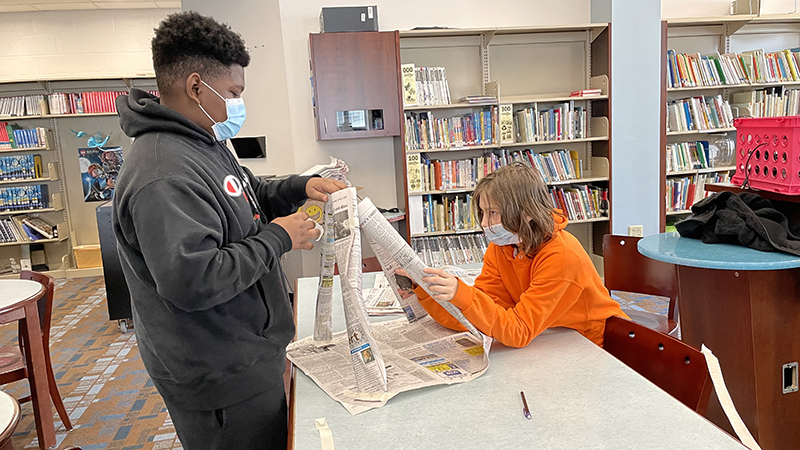 Two students build a tower out of newspaper.