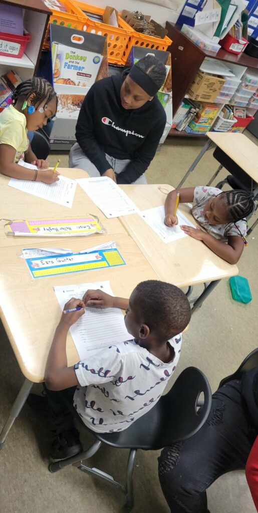 An eighth grader watches over first graders as they complete their work.