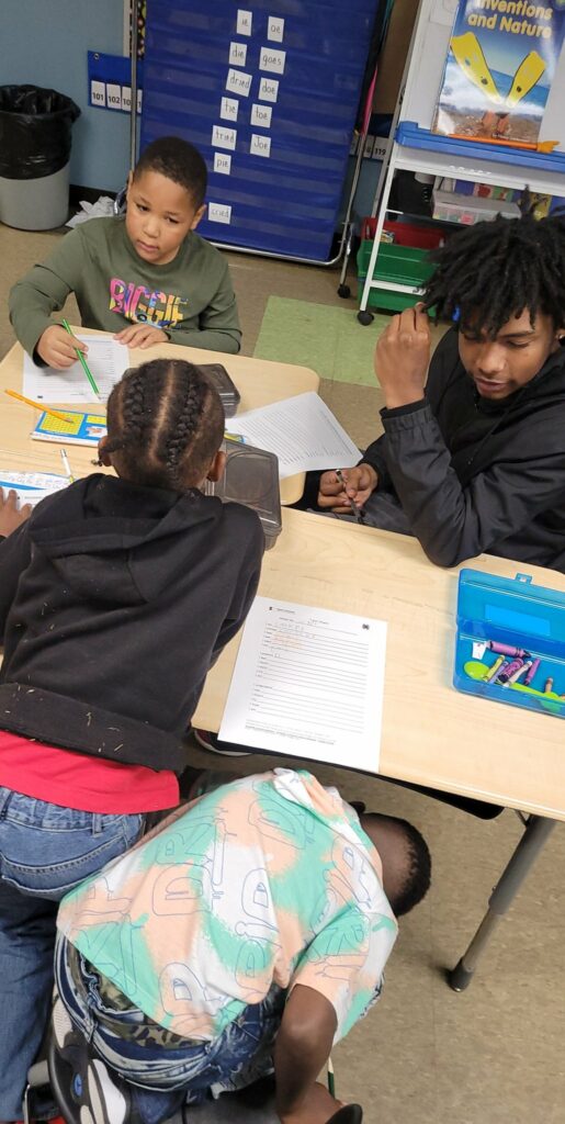 First graders sitting with an eighth grader as they work.