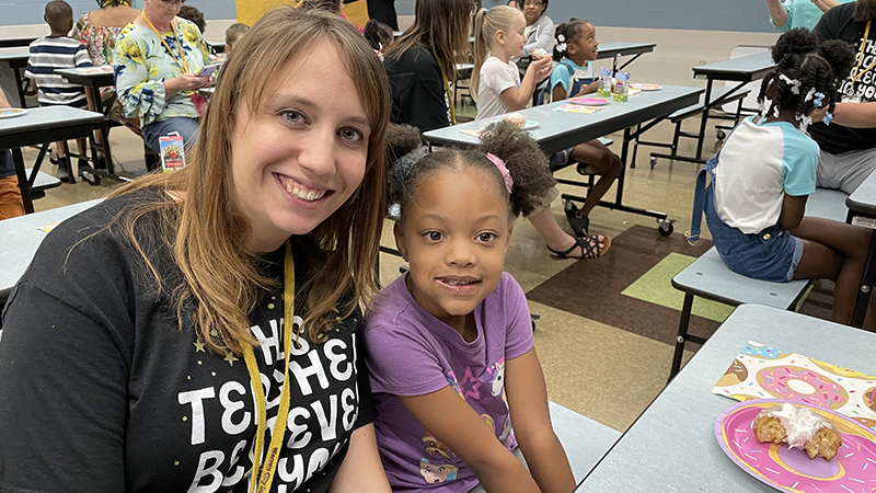 A kindergarten student enjoys her donut award with Mrs. Sauer.