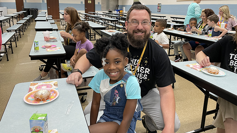 A first grader celebrates her donut award with Mr. Bitner.