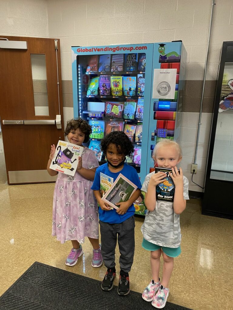 three students showing the books they chose from the vending machine