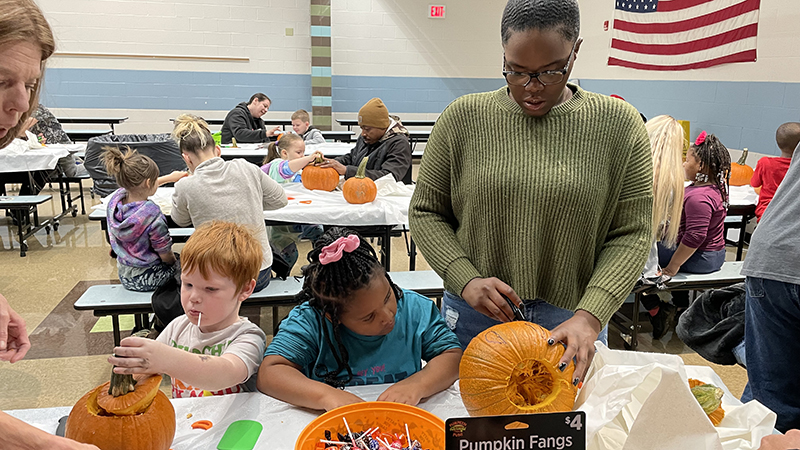 A helper draws a face on a student's pumpkin.