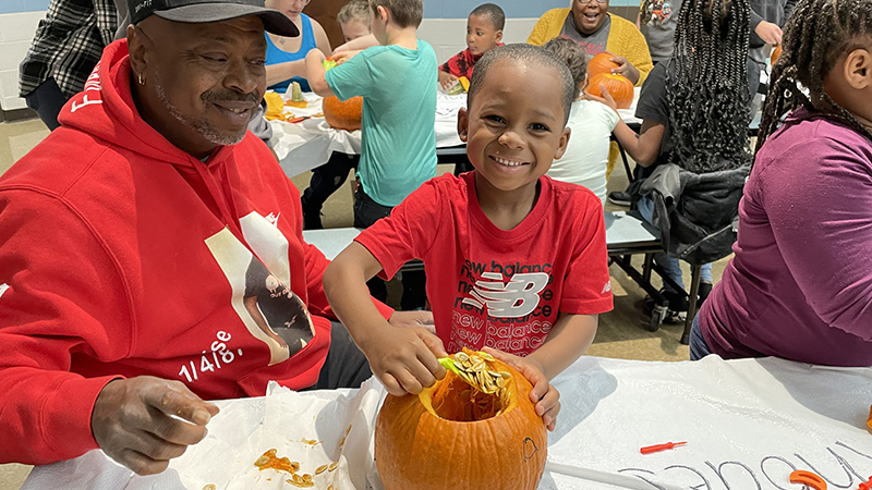 A student is all smiles as he scoops out his pumpkin.