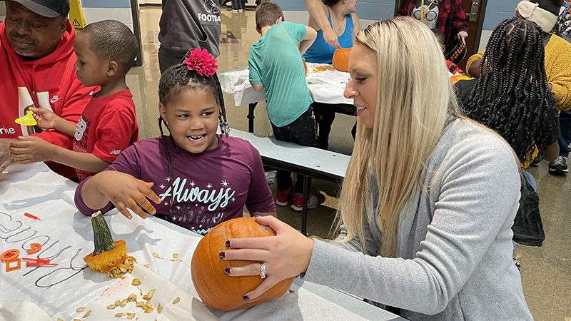Mrs. Tamburro helps a student carve her pumpkin.