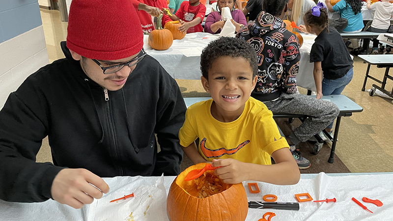 A student smiles as he helps to clean his pumpkin.