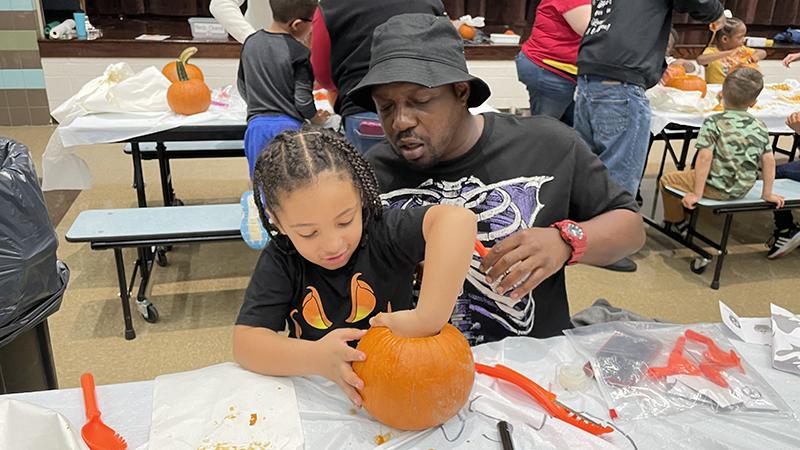 A student cleans his pumpkin as his helper looks on.