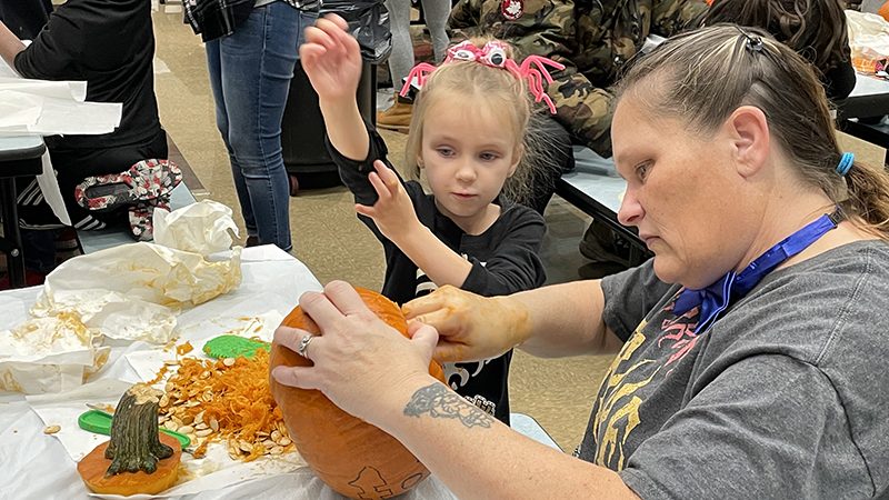 A student watches on as her helper starts carving her pumpkin.