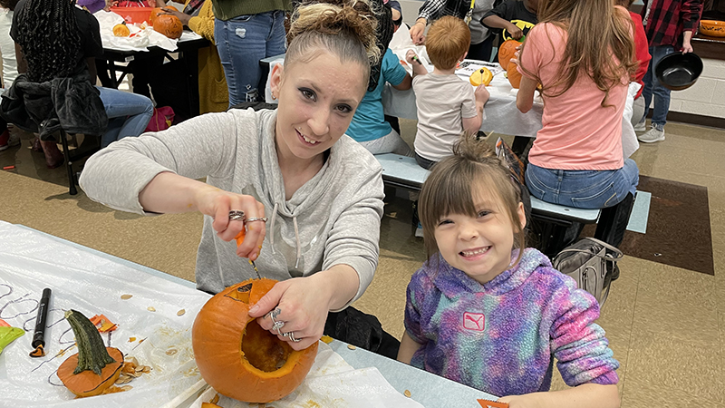 A student and her helper carving their pumpkin.