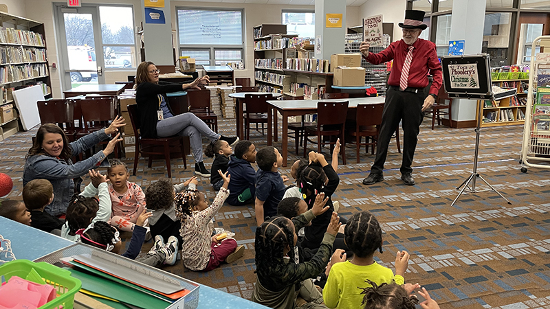 Students raise their hands to help with a magic trick.