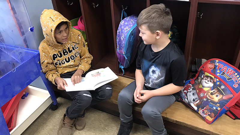 A kindergarten student listens as his fourth grade buddy reads to him.