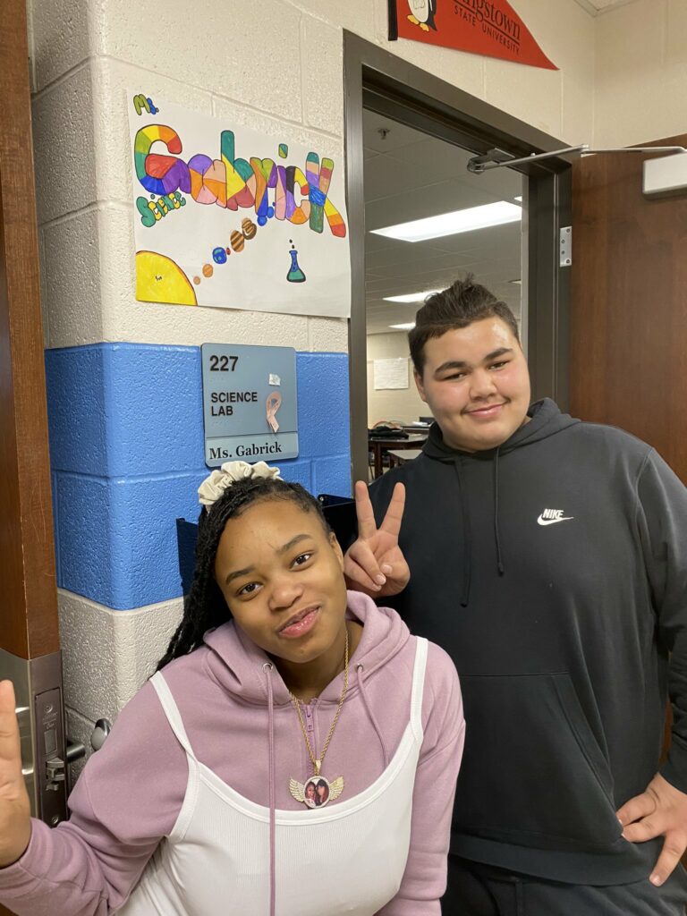 Two middle school students show a poster they helped create with the name of a teacher.