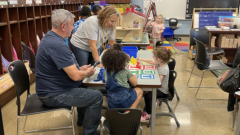 Mrs. Roberts shows a color activity to a student and their special guest.