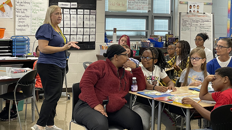 Students and guests listen as Mrs. Ulrich explains a math activity.