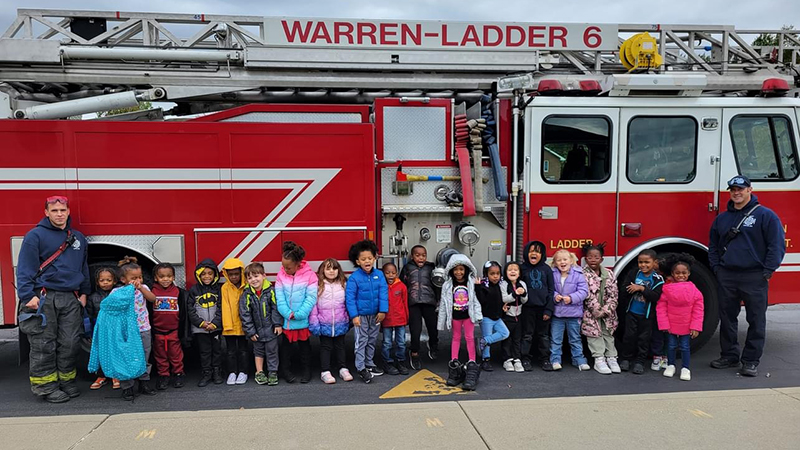 Students and firemen stand in front of fire truck for a picture