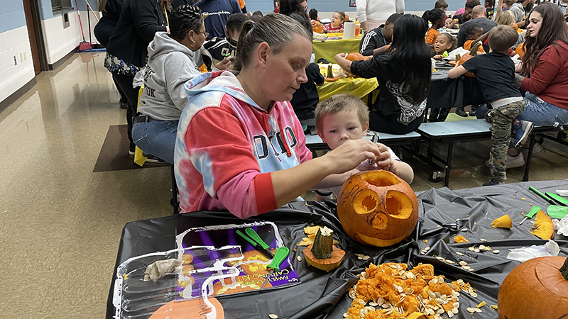 A kindergartener and his guest work together on their pumpkin.