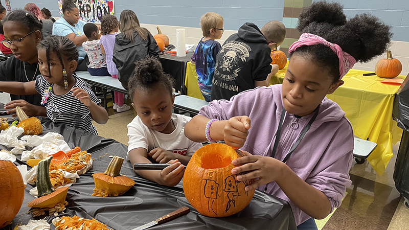 A student council member helps carve a pumpkin.
