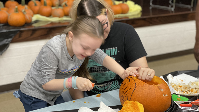 A kindergarten student carves her pumpkin.