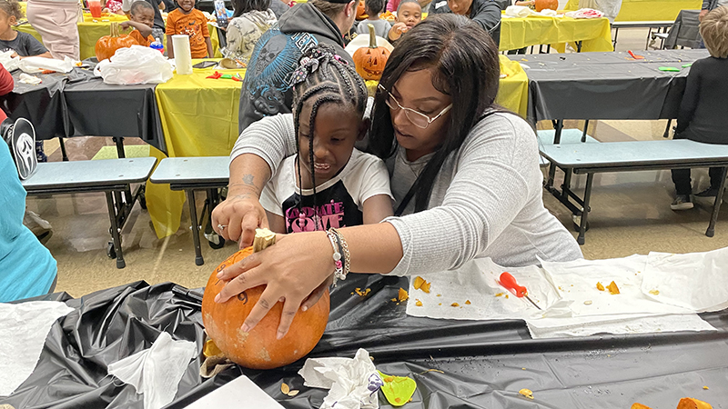 A kindergartener and her guest work together on their pumpkin.