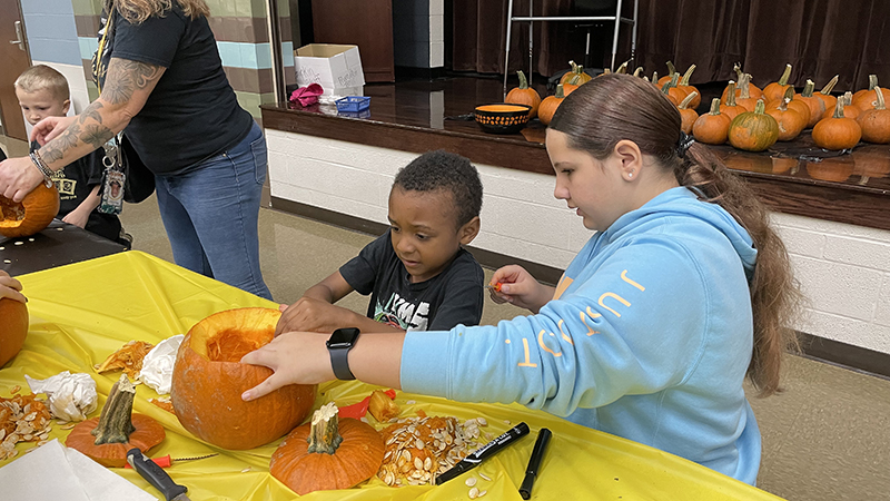 A student council member helps carve a pumpkin.