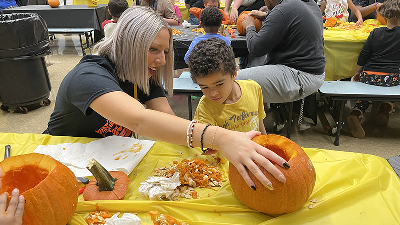 Mrs. Tamburro helps a student as they carve a pumpkin.