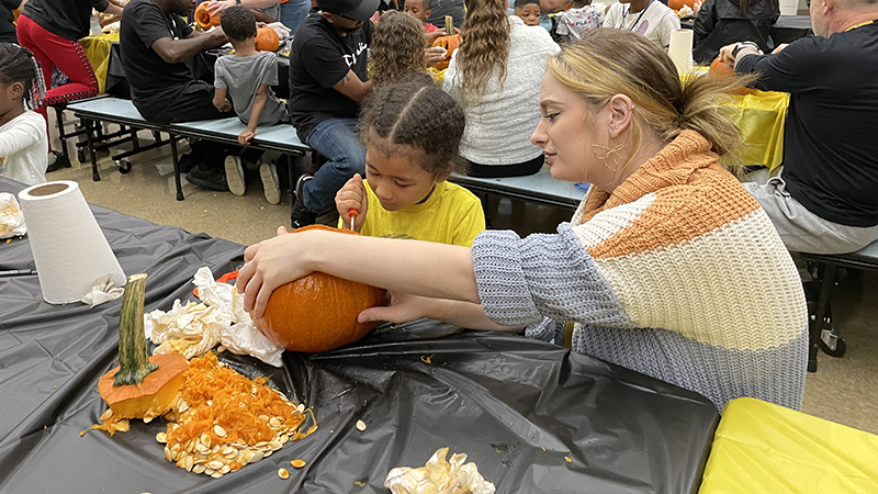 Miss Adams helps a student as he carves his pumpkin.