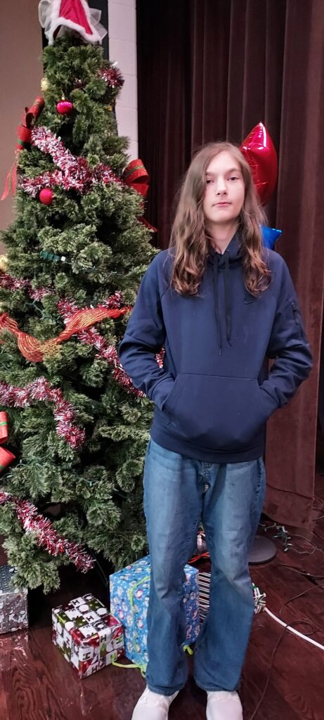 geography bee winner stands in front of Christmas tree.