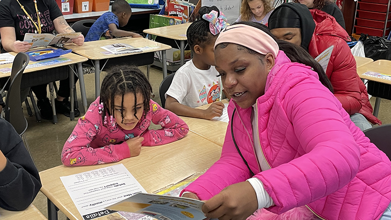 A guest reads a story to her student.