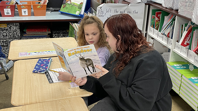 A guest reads a book to their student.