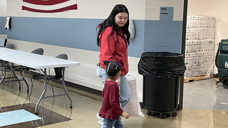 A student helper brings another student carry her gifts to the classroom.