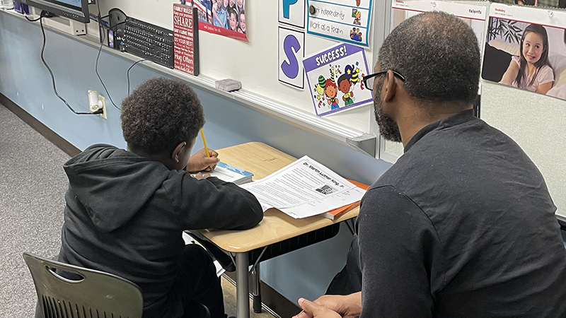 A guest looks on as his student completes his work.