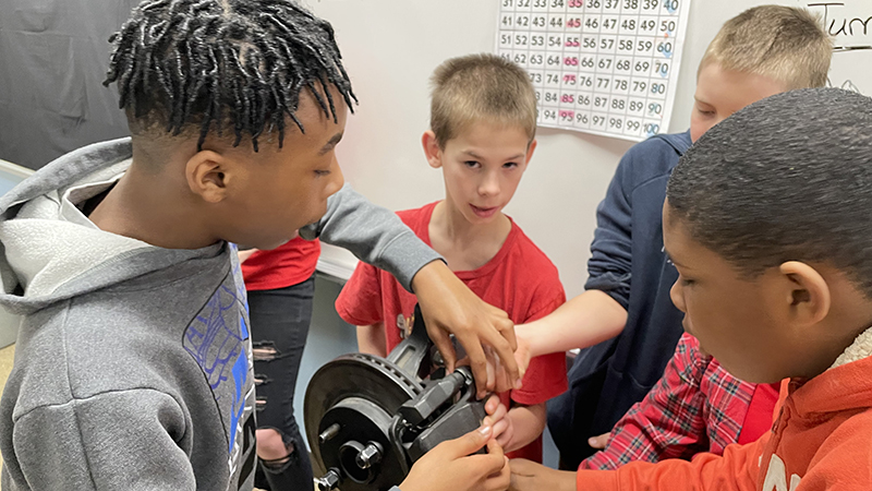 Students work together on various car parts to try to repair them.