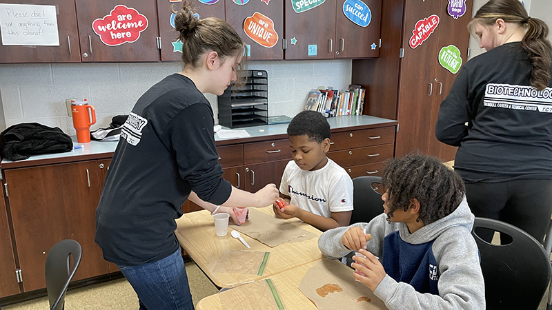 A TCTC student helps a student with his slime mixture.