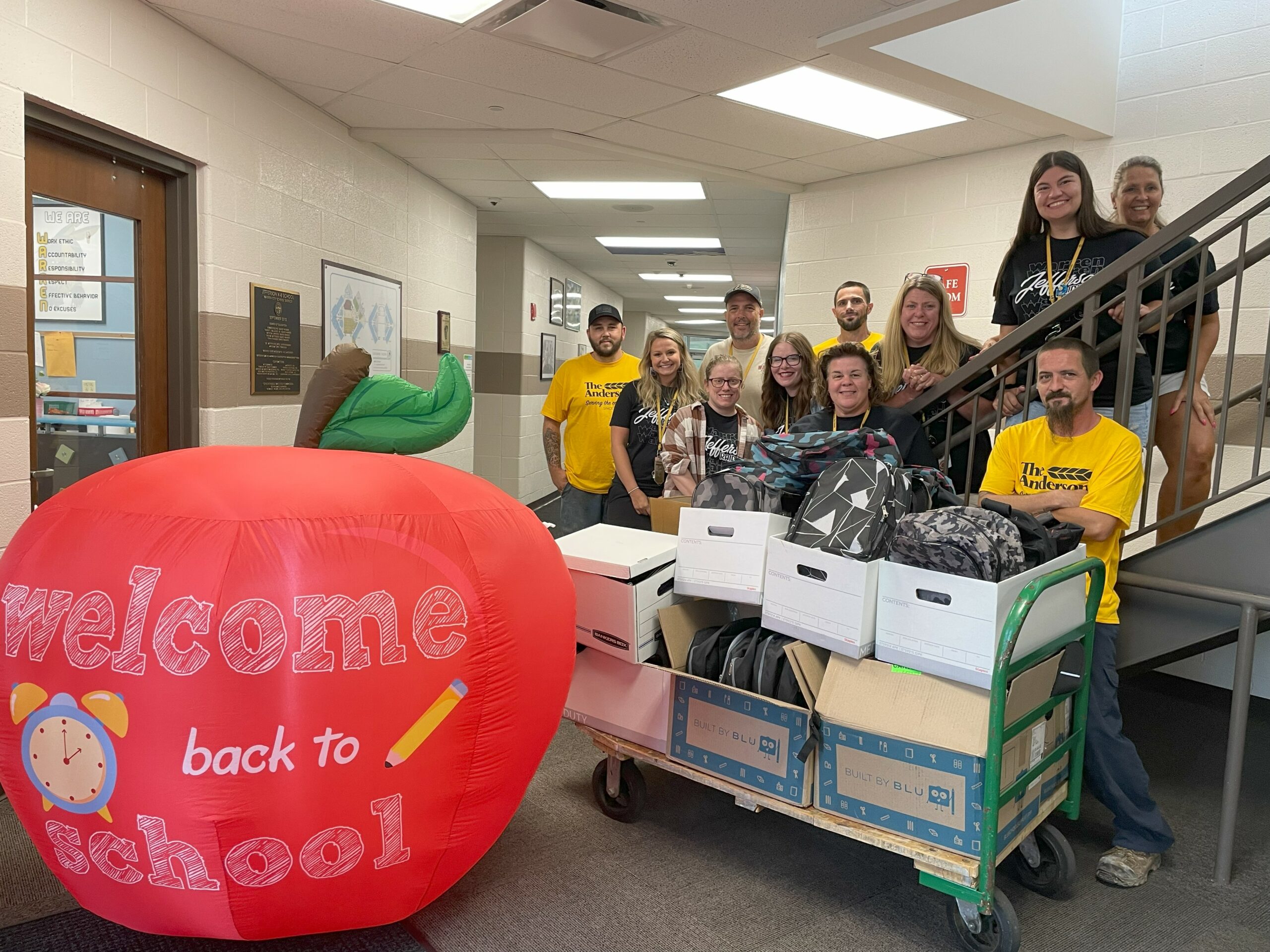 A group of teachers stand with workers from the Anderson company in front of backpack donations.