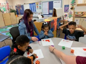 Parent with 4 preschoolers doing a math project at a table