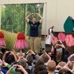 Students in a gym setting sitting on the floor watching a science lesson put on by COSI