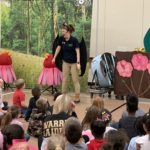 a presentor wearing bat wings in front of an assembly of students