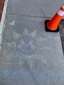 chalk drawing on sidwalk of sun with text saying we are in this together
