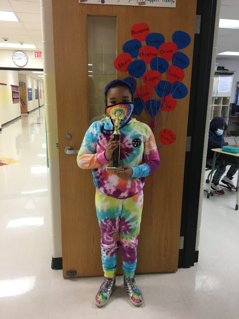 student: girl standing in front of an open classroom door