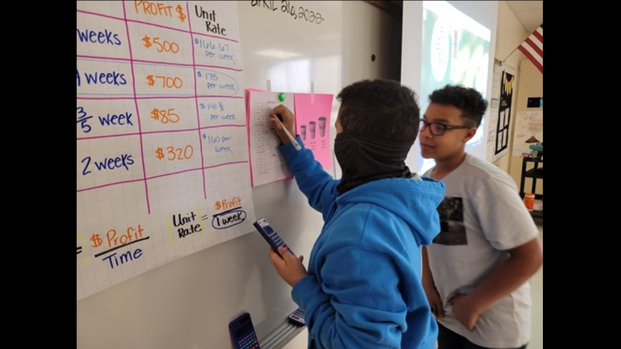 Two 6th grade boys figuring out a problem on a white board