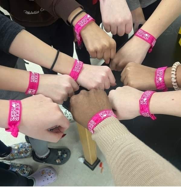 fists in a circle with pink bracelets on